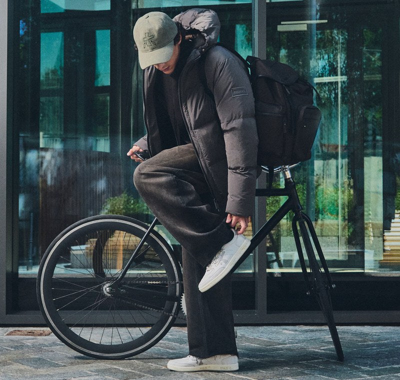 Man on a bicycle in white Premiata sneakers, with a close-up of the shoe on the pedal. Photo @premiataofficial